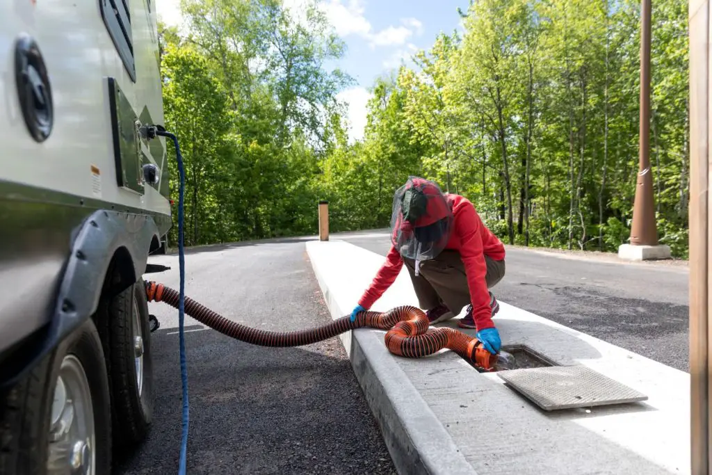 how to dump your RV waste tanks: photo shows a person connecting RV sewer hose to dump their RV waste tanks