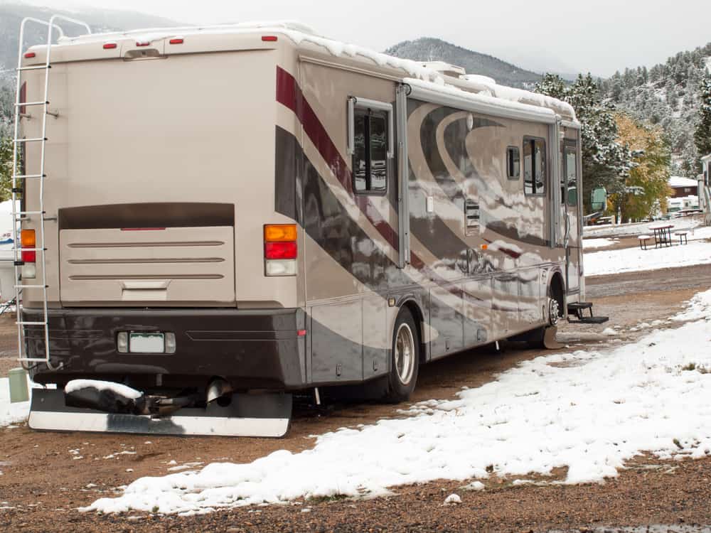 living in a motorhome in winter: image of a motorhome parked at a campground in winter time with snow covered mountains in the background
